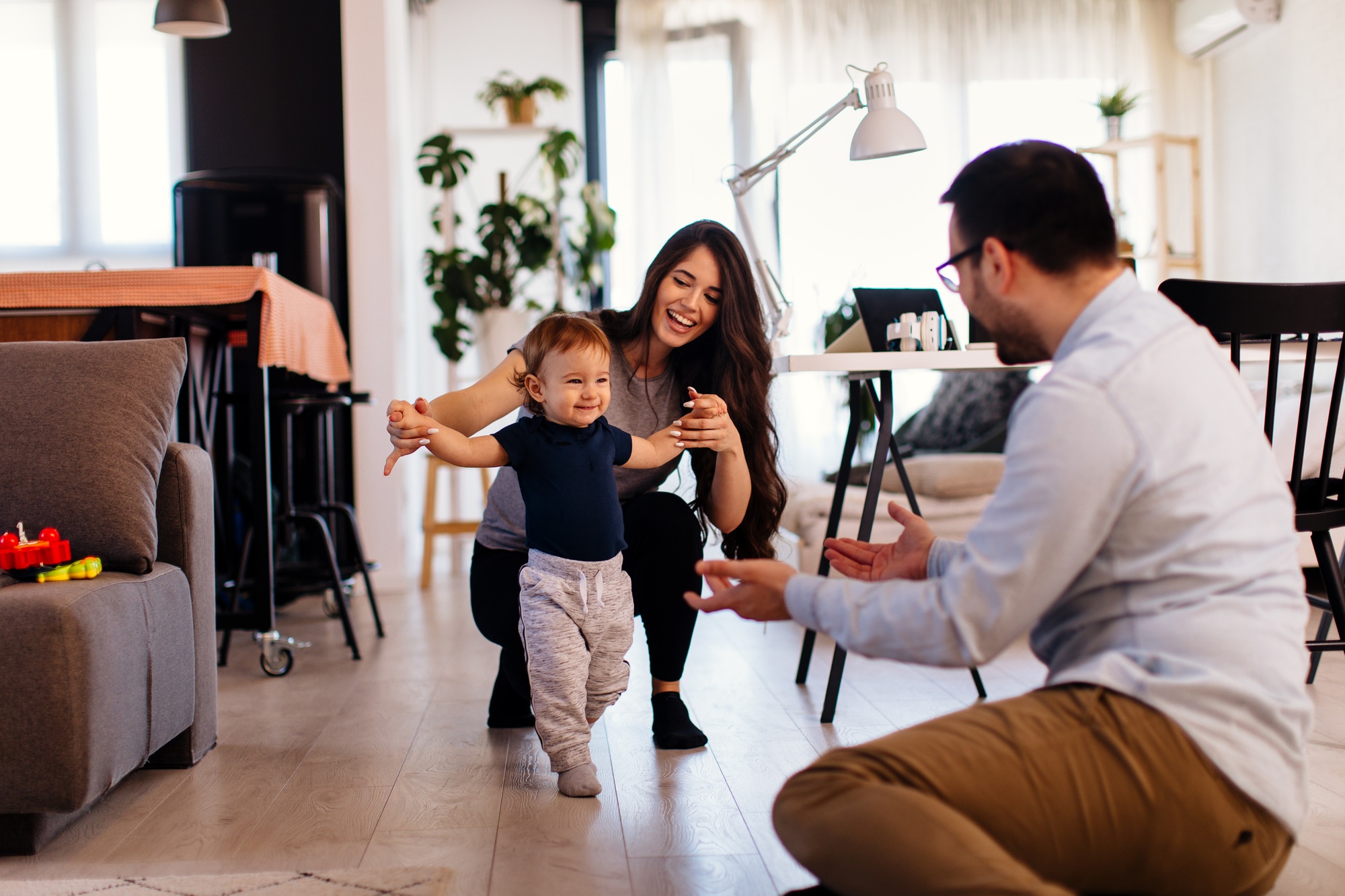 Young married couple teaching their son to learn the first baby steps in their home